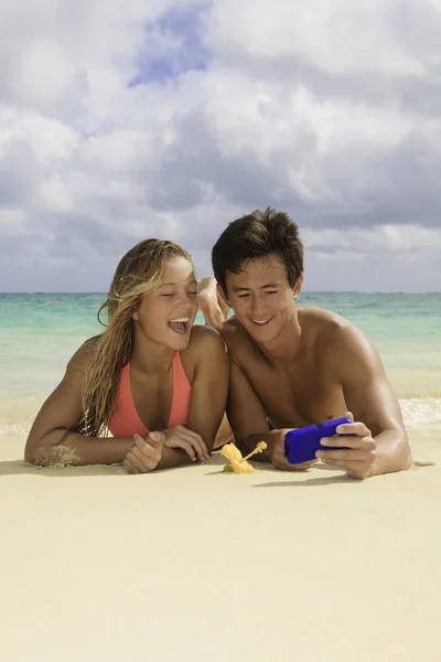 Couple on the beach in hawaii with their cell phone — Stock Photo, Image