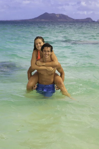 Couple chevauchant piggyback dans l'océan — Photo