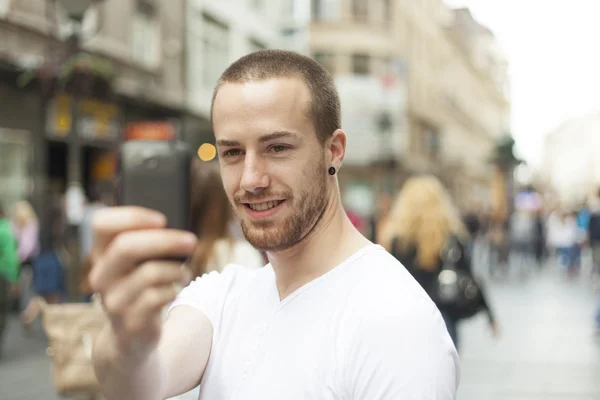 Улыбающийся парень на улице фотографирует с мобильного телефона — стоковое фото