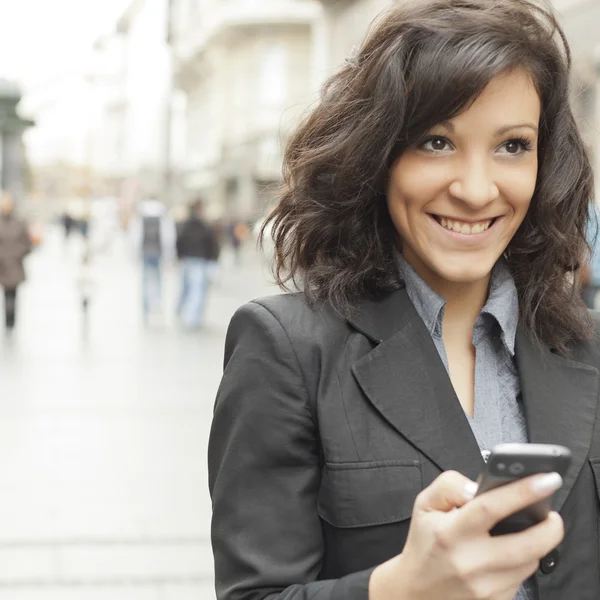Mujer joven con sonrisa y smartphone caminando por la calle —  Fotos de Stock