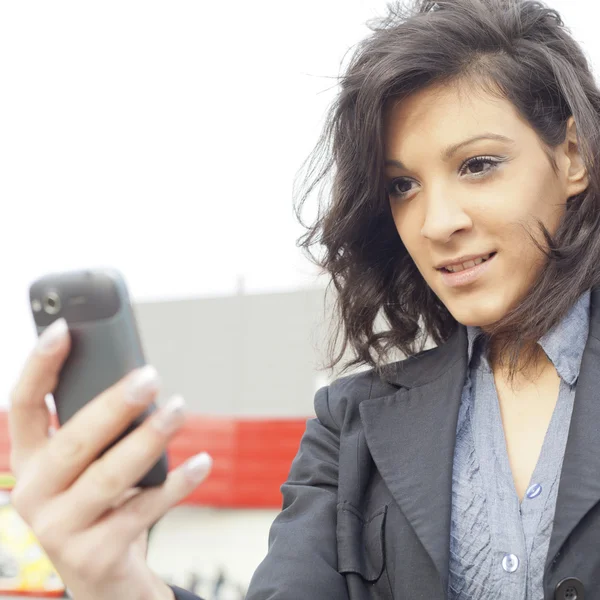 Jonge vrouw met mobiele telefoon wandelen, blured zakelijke gebouw in — Stockfoto