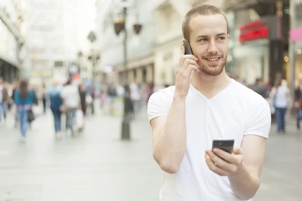 Мужчины, говорящие по одному мобильному телефону и держащие в руках секундовый телефон — стоковое фото