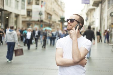 genç adam güneş gözlüğü ve caddede yürümek telefon