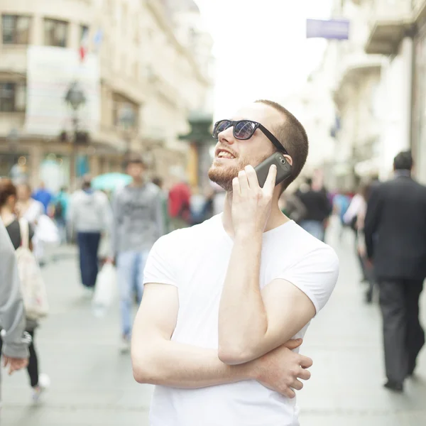 Ung man med solglasögon och mobiltelefon på gatan — Stockfoto