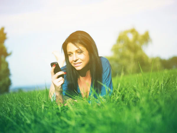 Jonge vrouw met mobiele telefoon in park — Stockfoto