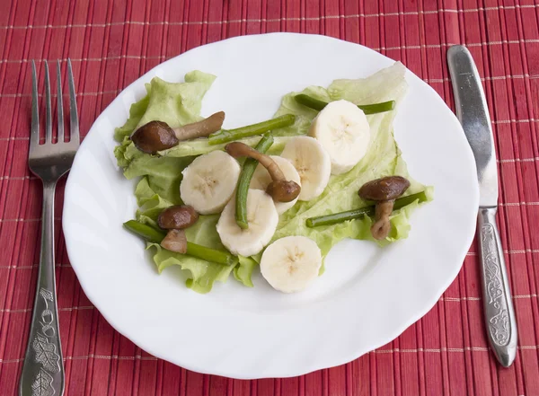 Creative salad from fried fungi and stalks of garlic and sweet bananas — Stock Photo, Image
