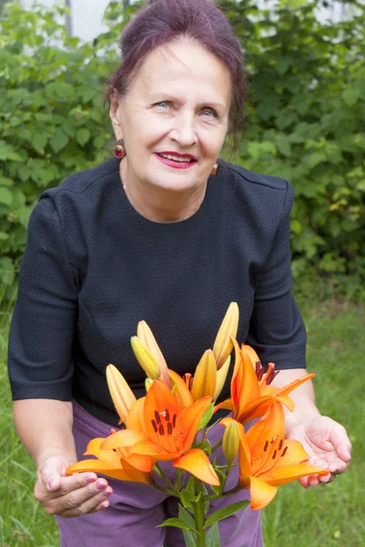 The happy smiling woman and orange flowers of a lily in a garden — Stock Photo, Image