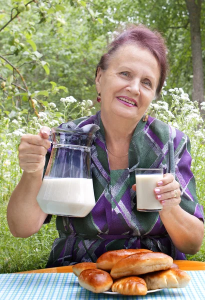 Η ευτυχής ηλικιωμένη γυναίκα τρώει πίτες με φρέσκο γάλα — Φωτογραφία Αρχείου