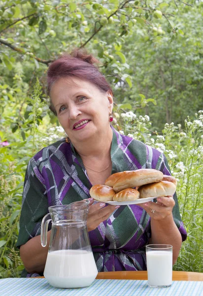 La donna anziana felice mangia torte con latte fresco — Foto Stock