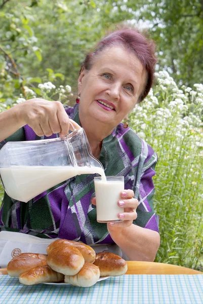Mutlu bir yaşlı kadın pies taze süt ile eats — Stok fotoğraf