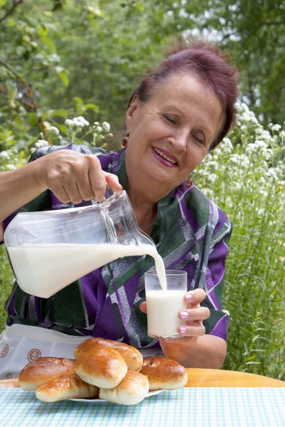 De gelukkig volwassen vrouw eet taarten met verse melk — Stockfoto