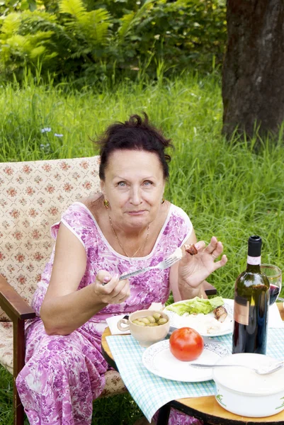 De volwassen vrouw heeft diner in een groene zomertuin — Stockfoto