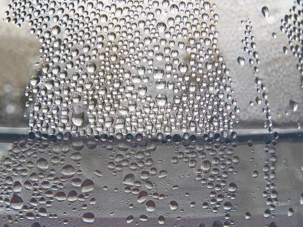 Einfarbige Wassertropfen auf einer transparenten Glasoberfläche. — Stockfoto