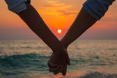 pár drží za ruce na moři při západu slunce