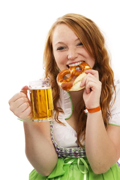 Redhead woman in bavarian dress with beer eating pretzel — Stock Photo, Image