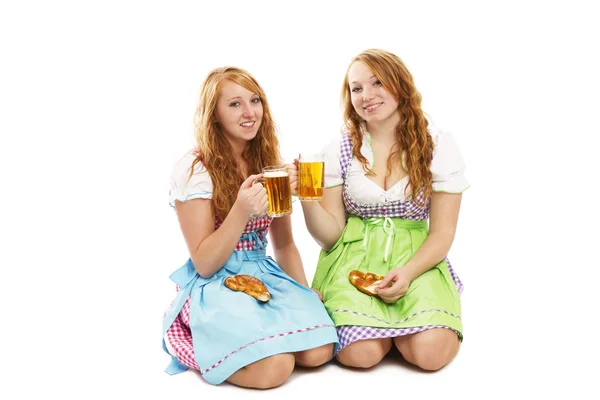 Two bavarian girls with pretzels and beer kneeling on floor — Stock Photo, Image