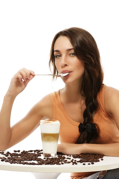 Hermosa mujer con cuchara en la boca sentada en una mesa con café con leche macchiato —  Fotos de Stock