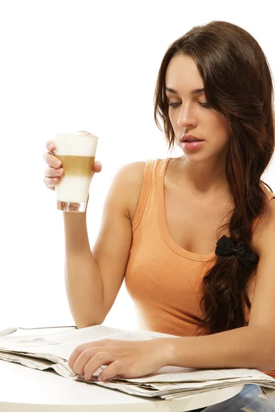 Jonge vrouw zitten aan een tafel lezen krant bedrijf latte macchiato koffie — Stockfoto