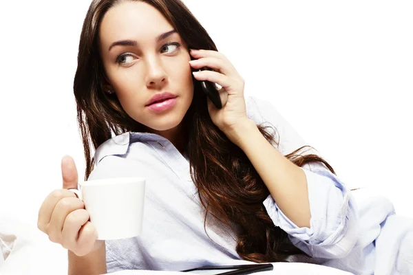 Mulher bonita na cama segurando café ao ligar com seu telefone — Fotografia de Stock