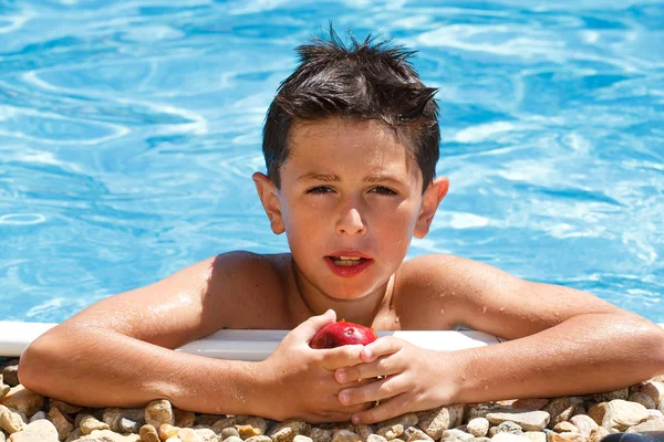 Мальчик ест фрукты в бассейне — стоковое фото