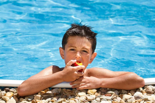 Мальчик ест фрукты в бассейне — стоковое фото