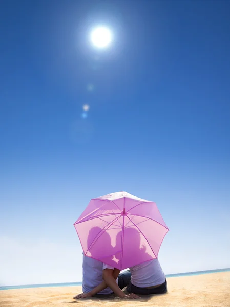 Пара поцелуев под зонтиком на пляже — стоковое фото