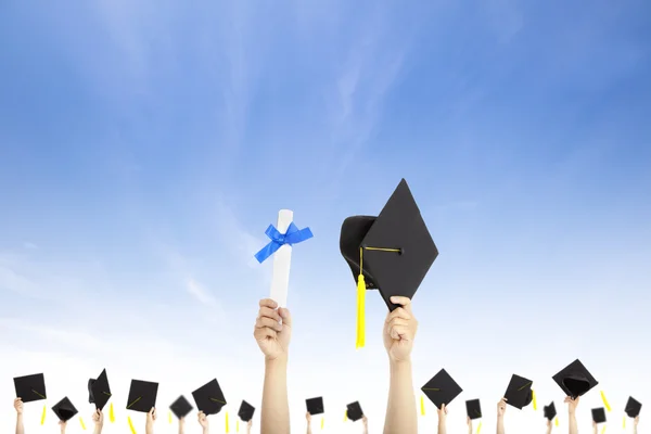 Ręka trzyma graduation czapki i dyplom certyfikat z chmura tła — Zdjęcie stockowe