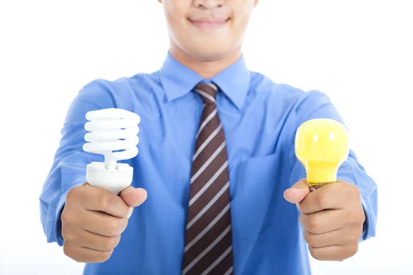 Улыбающийся бизнесмен держит энергосберегающую лампочку и традиционную лампочку — стоковое фото