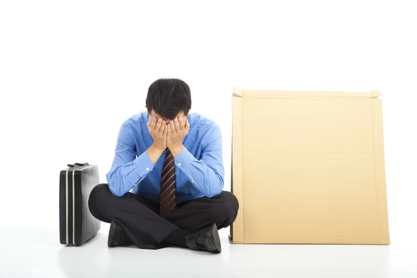 Frustrated businessman sitting on ground and blank cardboard Royalty Free Stock Images