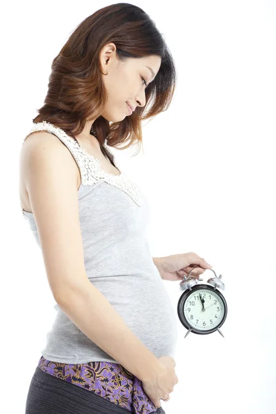 白で隔離される目覚まし時計を保持しているアジアの妊娠中の女性 — ストック写真