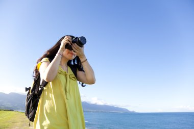 Young woman with backpack standing on the hill taking photo clipart