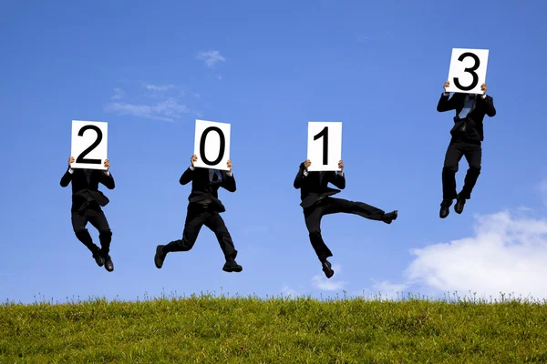 Бизнесмен проводит 2013 год и прыгает на зеленое поле — стоковое фото