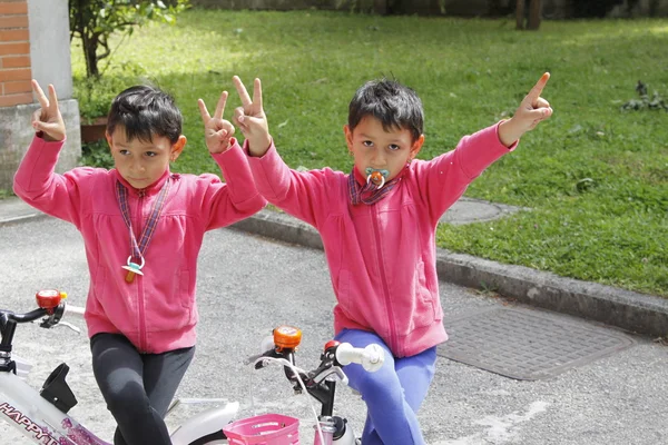 Två små tvillingar cykel med händerna upp — Stockfoto
