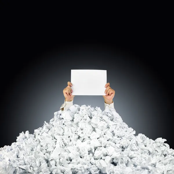 Person under crumpled pile of papers with hand holding a help si — Stock Photo, Image