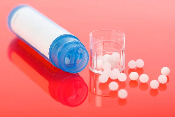 Comprimidos homeopáticos e recipiente em vermelho — Fotografia de Stock