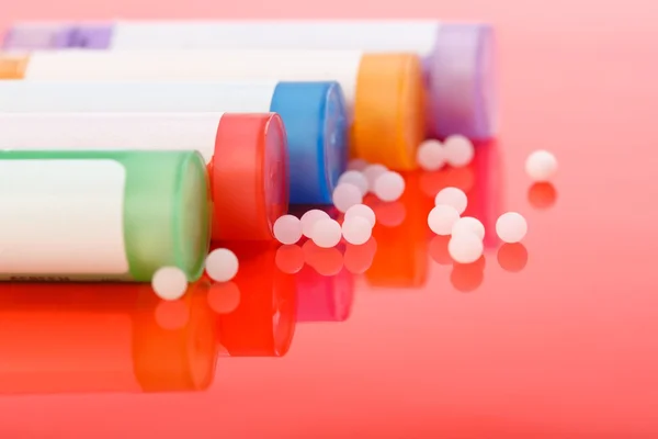 Pílulas homeopáticas coloridas e recipientes em vermelho — Fotografia de Stock