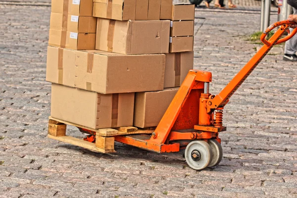 Courier shipping carboard boxes on a orange trolly, on stone floor — Stock Photo, Image