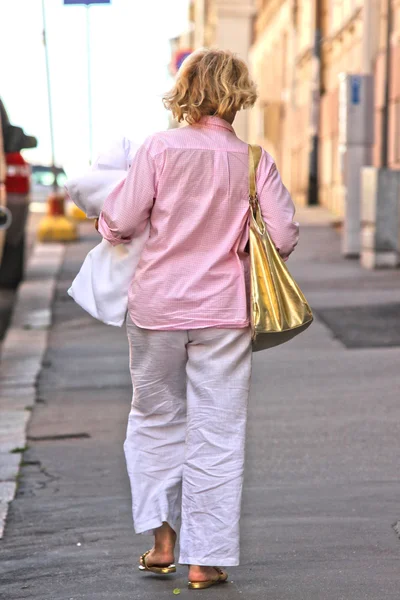 Пожилая женщина ходит по тротуару с золотым мешком — стоковое фото