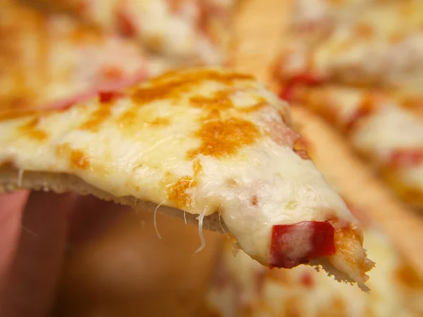 Scheibe Pizza, die von einer Person hochgehalten wird — Stockfoto
