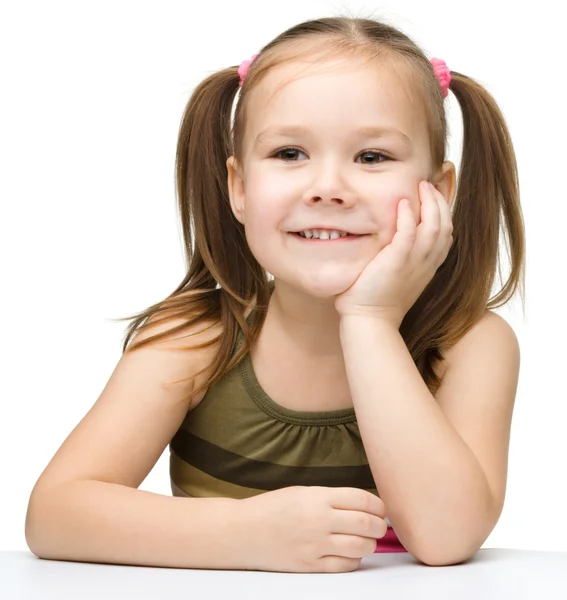 Gelukkig meisje zit aan een tafel en glimlach — Stockfoto