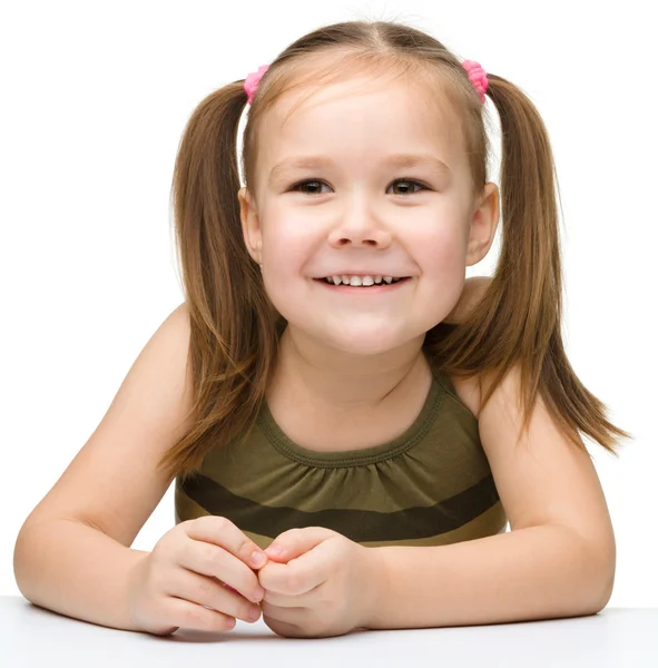 Glad liten flicka sitter vid ett bord och leende — Stockfoto