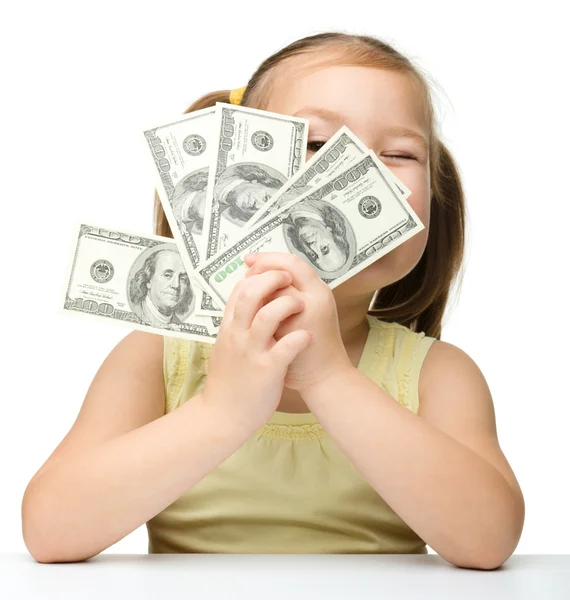 Cute little girl is covering her eyes with dollars — Stock Photo, Image