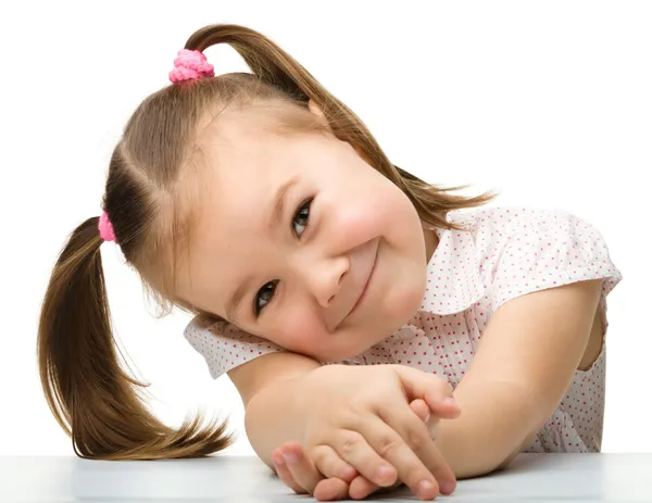 Menina feliz senta-se a uma mesa e sorri — Fotografia de Stock