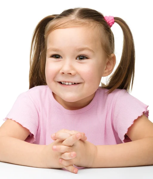 Joyeux petite fille assise à une table et sourire — Photo