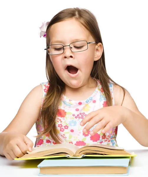 Cute little girl is yawning while reading book — Stock Photo, Image