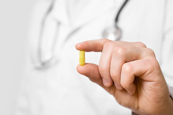 Доктор ізольований на сірому фоні, пропонуючи маленьку таблетку — стокове фото