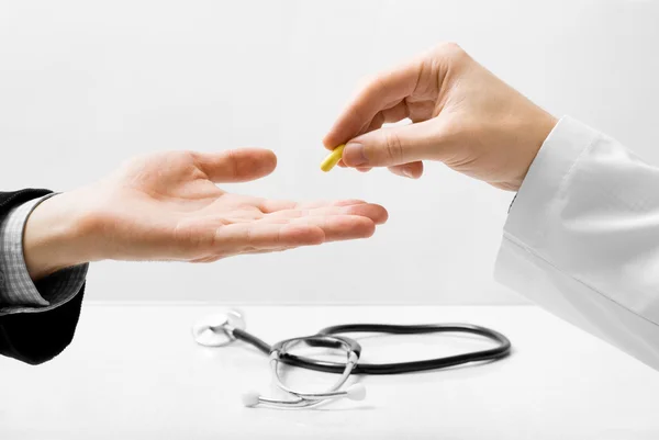 Доктор ізольований на сірому фоні, пропонуючи маленьку таблетку — стокове фото