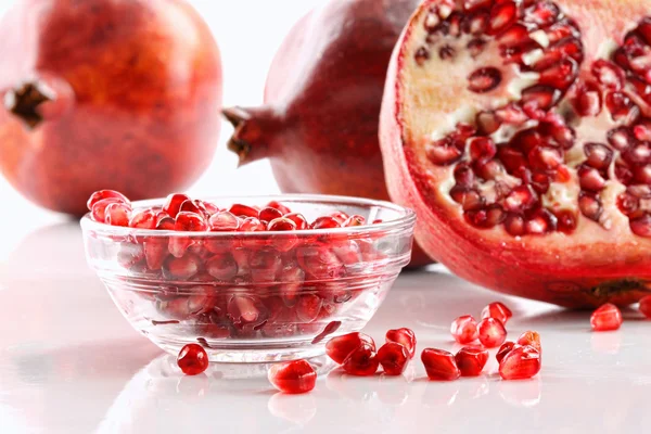 Ripe pomegranates and glass bowl of seeds on white — Stock Photo, Image