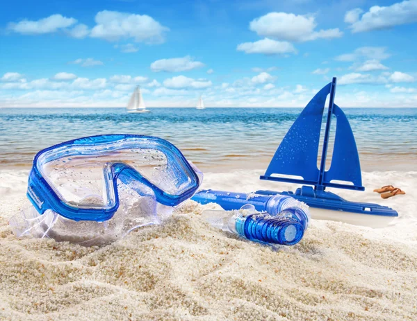 Goggles and toy sailboat in sand — Stock Photo, Image