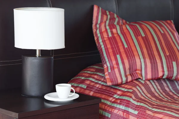 Bett mit Kissen, einer Tasse Tee auf dem Nachttisch und Lampe — Stockfoto